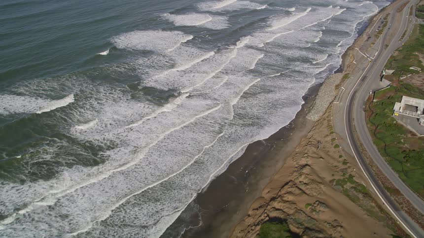 Aerial of waves rolling into a blacks sandy shoreline along the coast