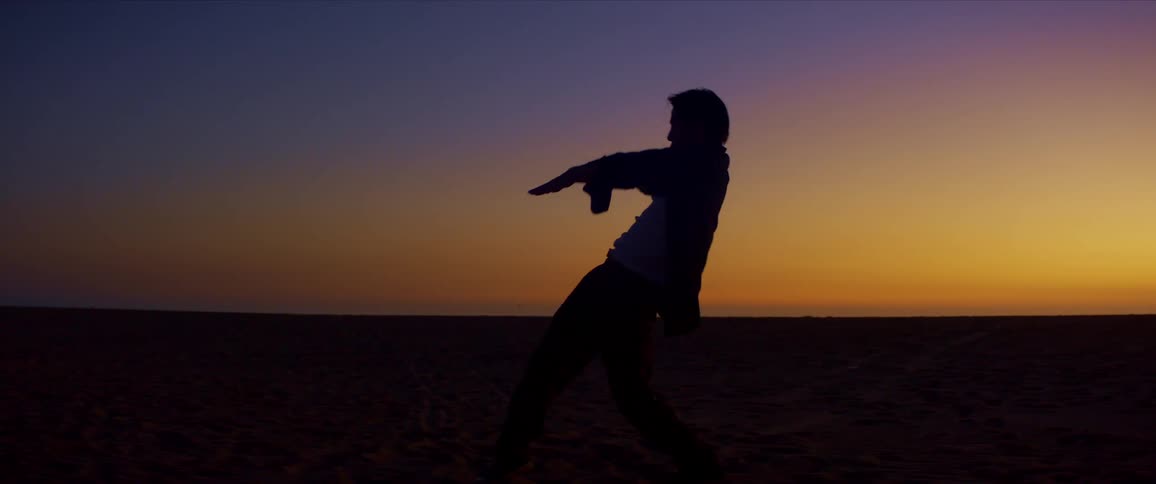 A male dancer is silhouetted against the sunset while dancing at the beach