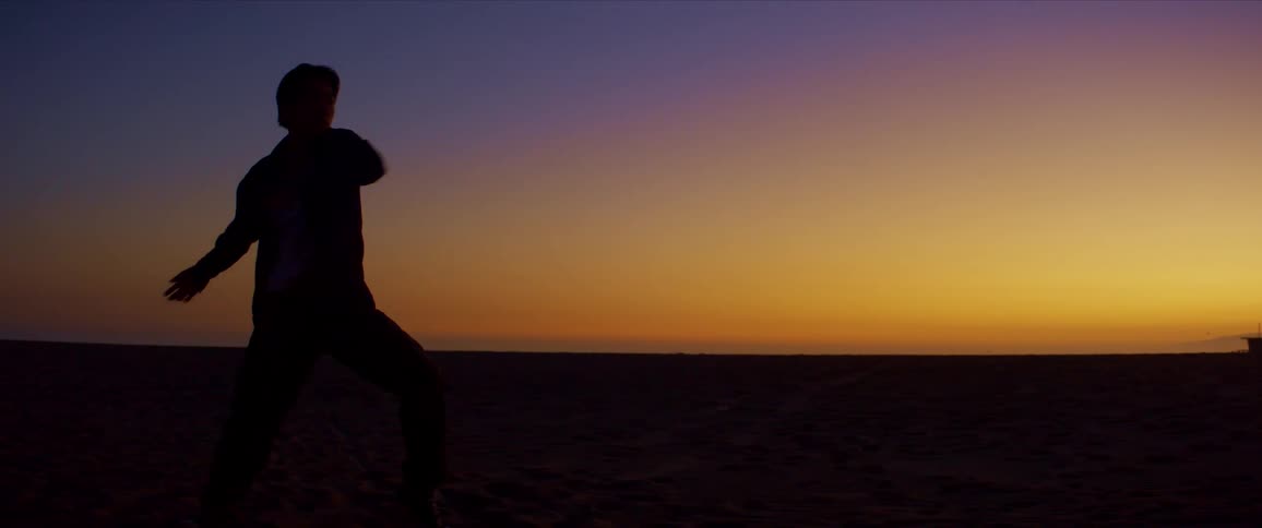 Silhouette of a man dancing on the beach against a yellow sky