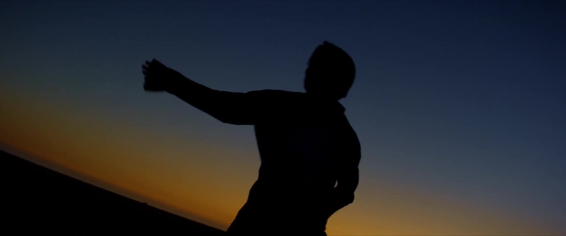 A male dancer is silhouetted against the sunset while dancing
