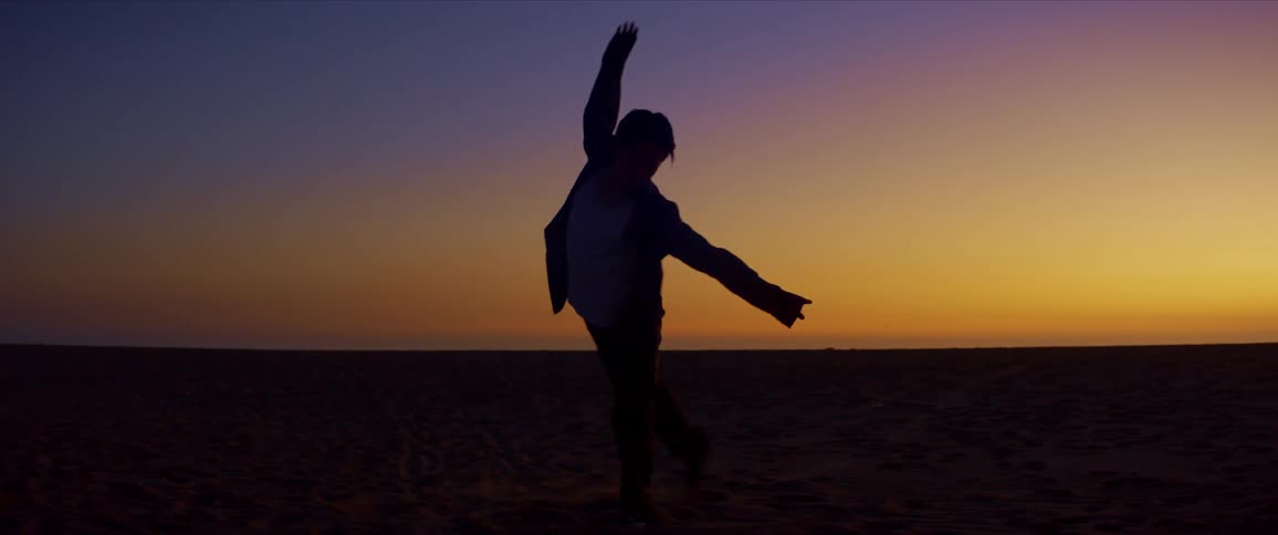 Silhouette of a man moving his body in the form of a dance on the beach sand against the red sky