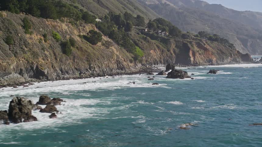 The powerful waves crash against the rocky shoreline on a sunny day sending plumes of spray high into the clear blue sky