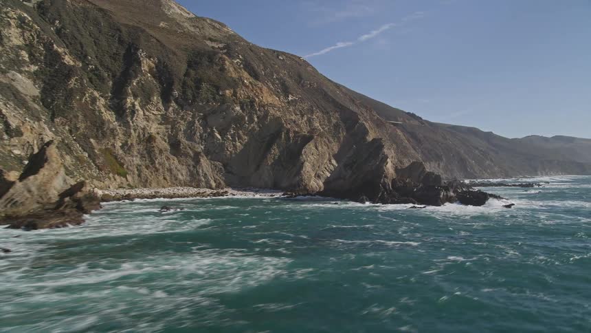 Turbulent blue sea meets rock formations at the base of steep cliffs