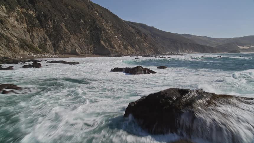 Landscape of a sea with waves hitting rocks on the edge of the mountainous coast