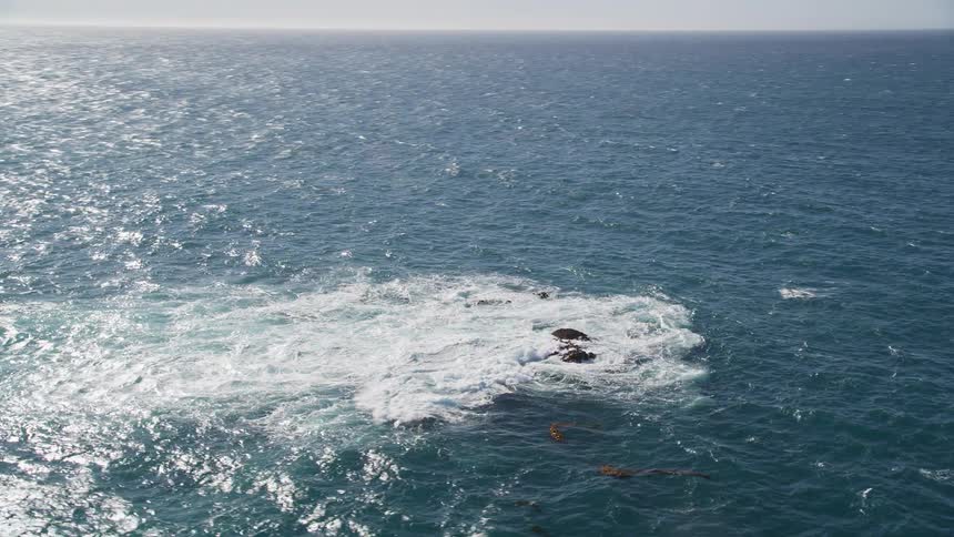 Vast ocean with rocks and waves building up with foam against the coast with mountains