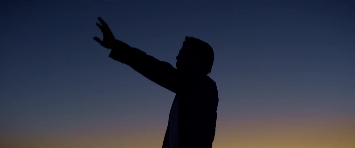 Silhouette of a man raising his arm and dancing against a dark dawn sky