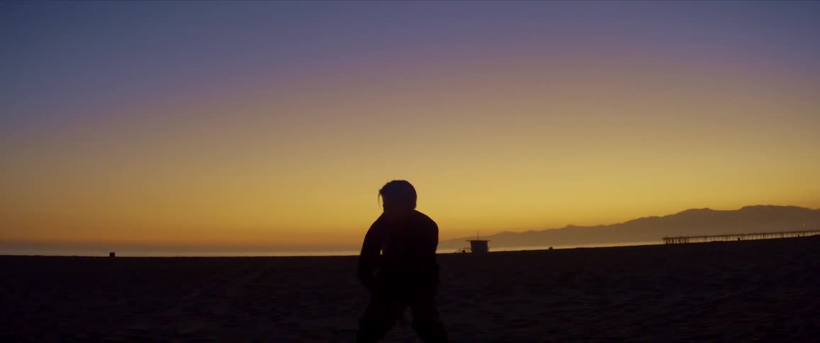 Silhouette of a man dancing on the beach sand against an orange and reddish sky