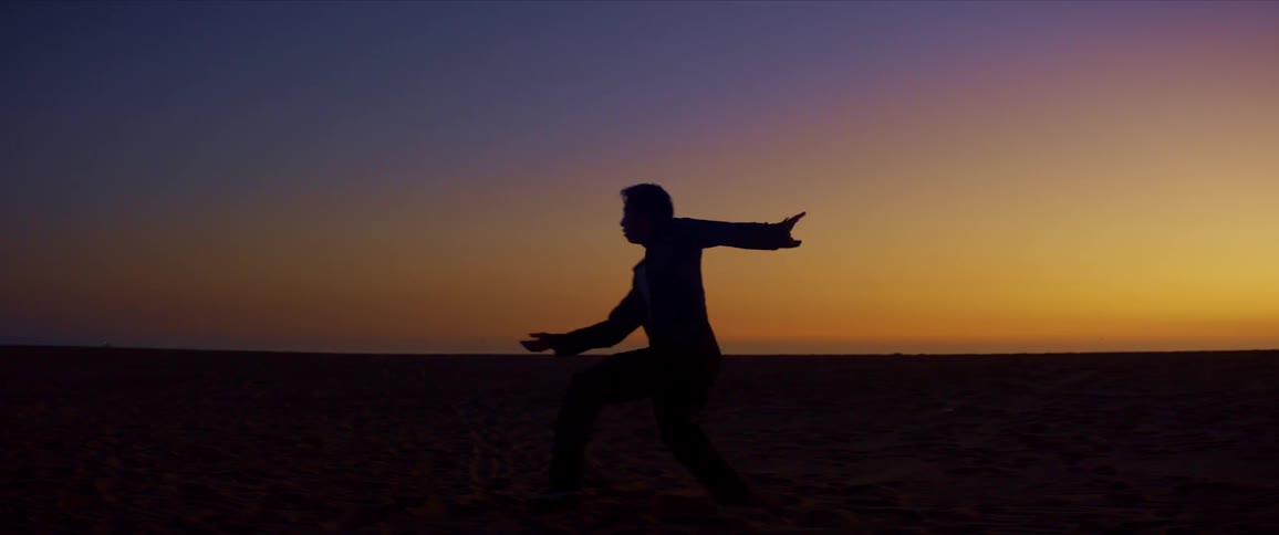 Silhouette of a man dancing on the beach sand on a yellowish morning sky