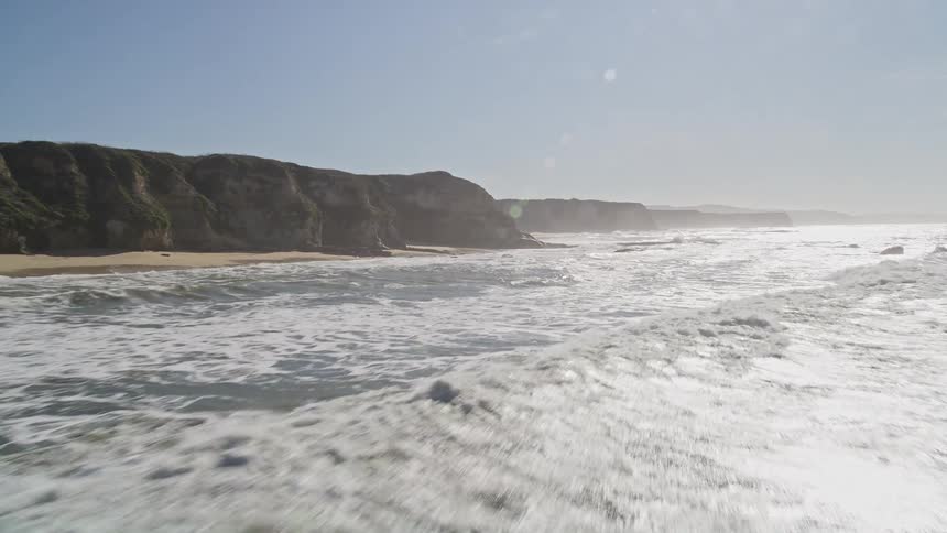 Landscape of waves on a beach hitting the rocky shore during a clear day