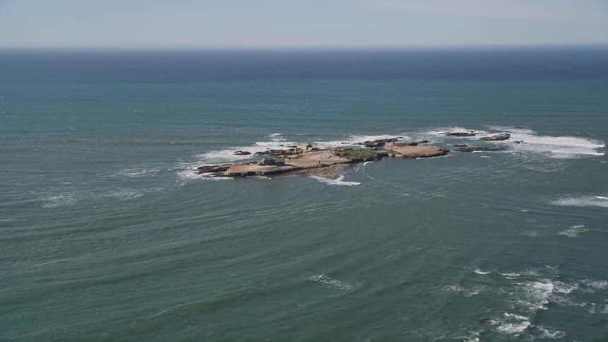 The small rocky islandof ao nuevo islandrests alone in the vast blue pacific ocean with crashing waves foaming around its shores