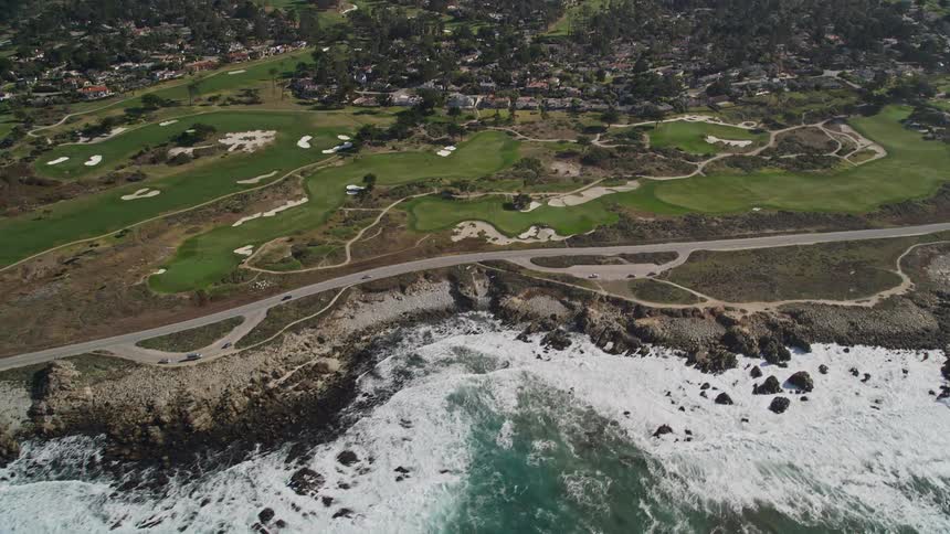 Aerial of ocean waves breaking against the shore near a highway and a city