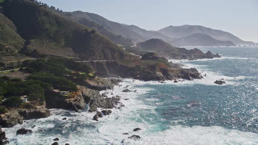 Traffic drives along coastal road bordering the mountains on a hazy day