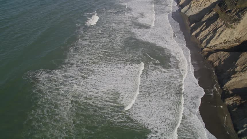 Foaming waves flow onto the beach at the base of coastal mountains