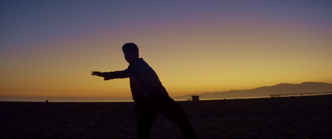 Silhouette of a man dancing on the beach sand in a sunrise with the golden sky