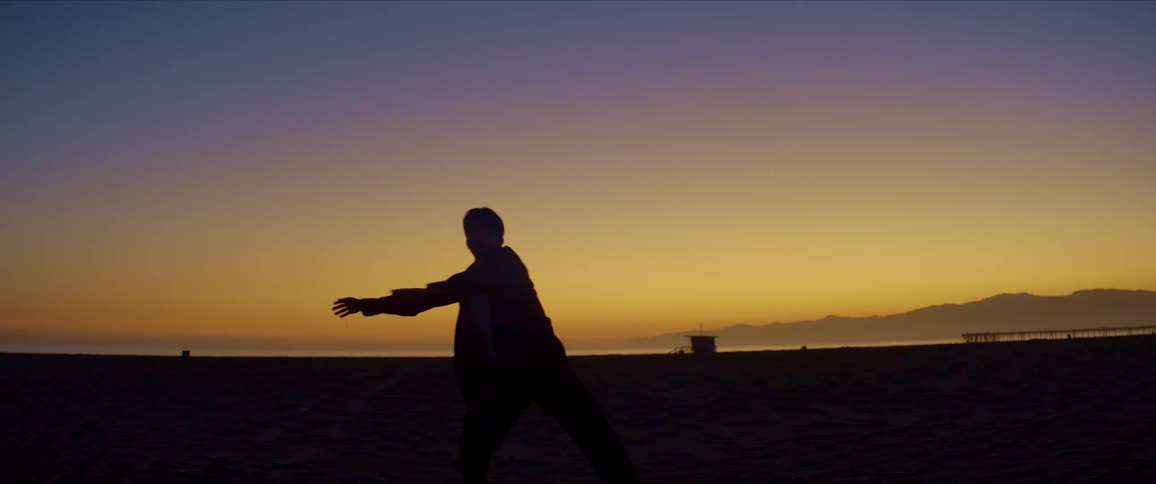 Silhouette of a person dancing on the beach sand with mountains on the horizon against a blue sky