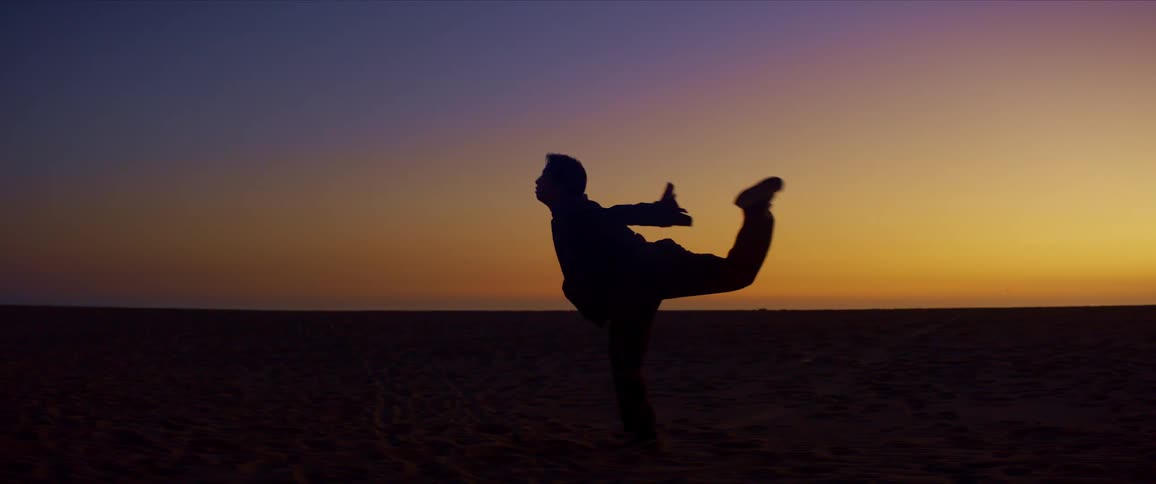 Silhouette of a man dancing on the beach sand on a yellow sky day
