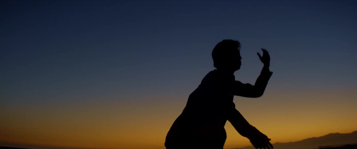 Silhouette of a man moving his arms and dancing against a blue and red sky