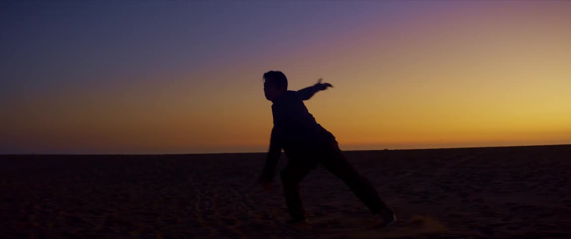 A male dancer is silhouetted against the sunset while dancing at the beach