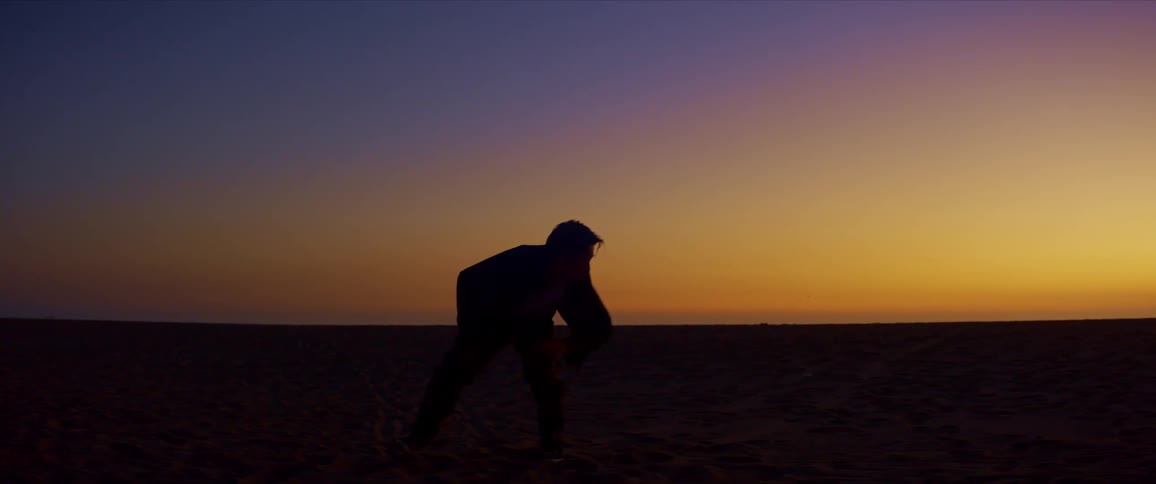 Silhouette of a person dancing on the beach sand against a reddish sky