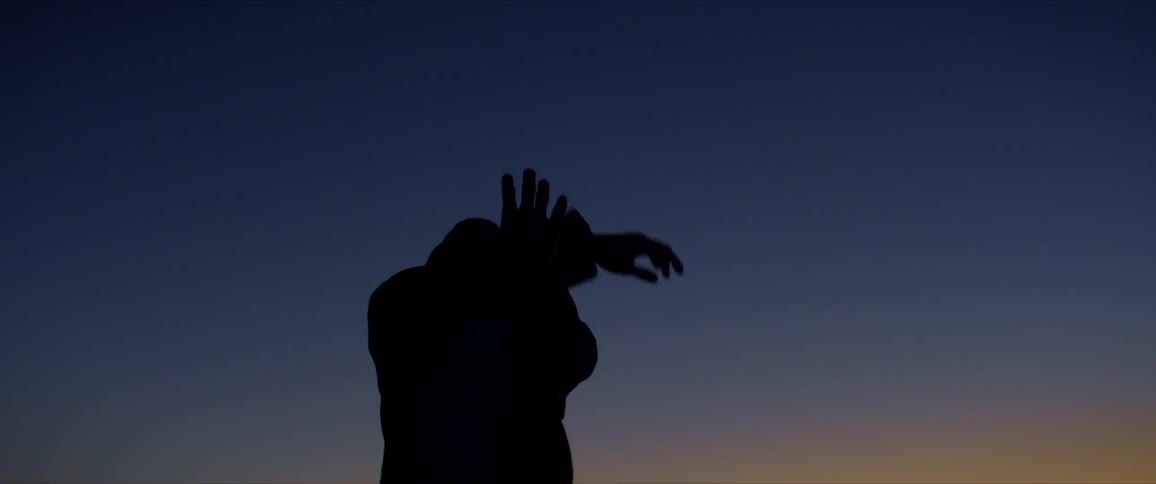 Silhouette of a man dancing outdoors against a blue late afternoon sky