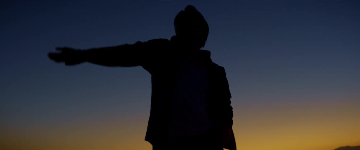 Silhouette of a man moving his arms while dancing outdoors against a blue and yellow background
