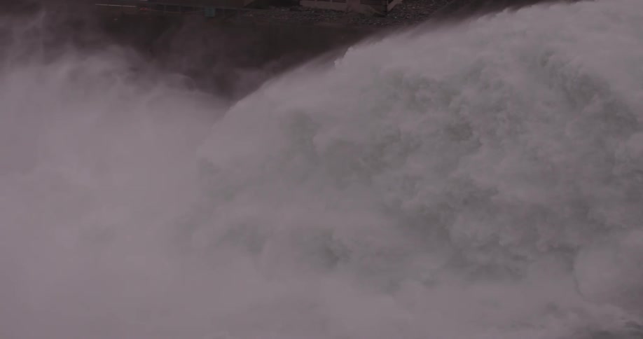 Torrential water flows from dam foaming and filling the air with mist