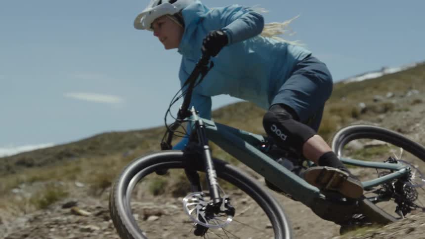 Blonde woman rides mountain bike down slope on a cloudy day