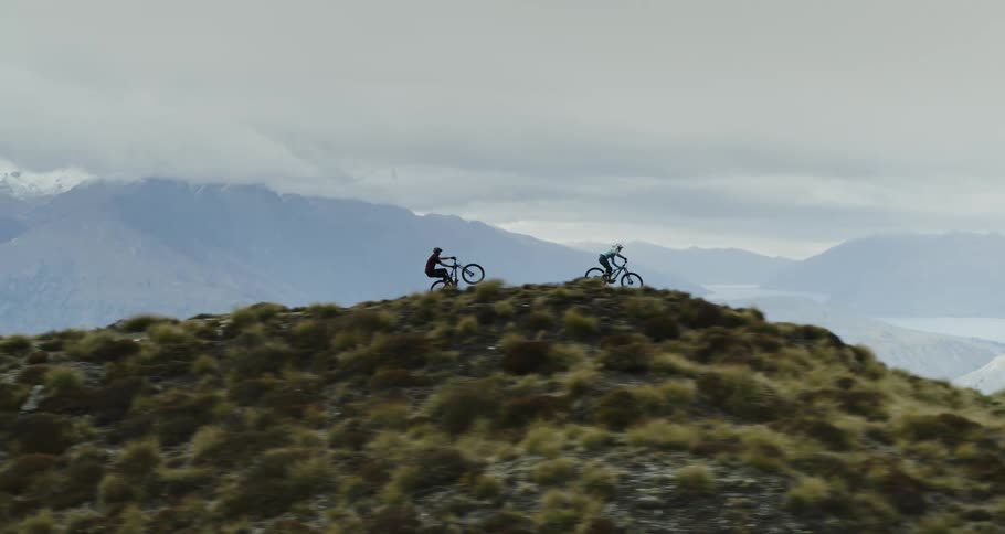 Two cyclists ride their mountain bikes down a grassy mountain top
