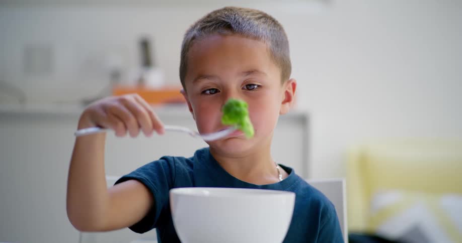 Little boy sitting picking up broccoli with a fork from a bowl