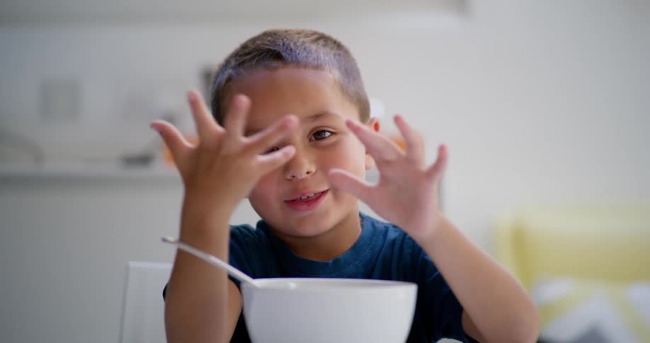 Portrait of a little boy playing with his fingers sitting at the table with a bowl in front of him