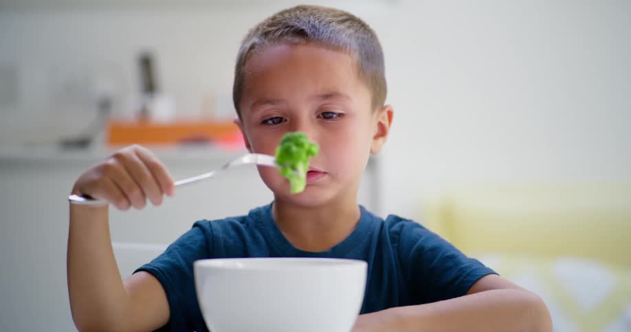 Young boy picking up broccoli from bowl and gagging in disgust