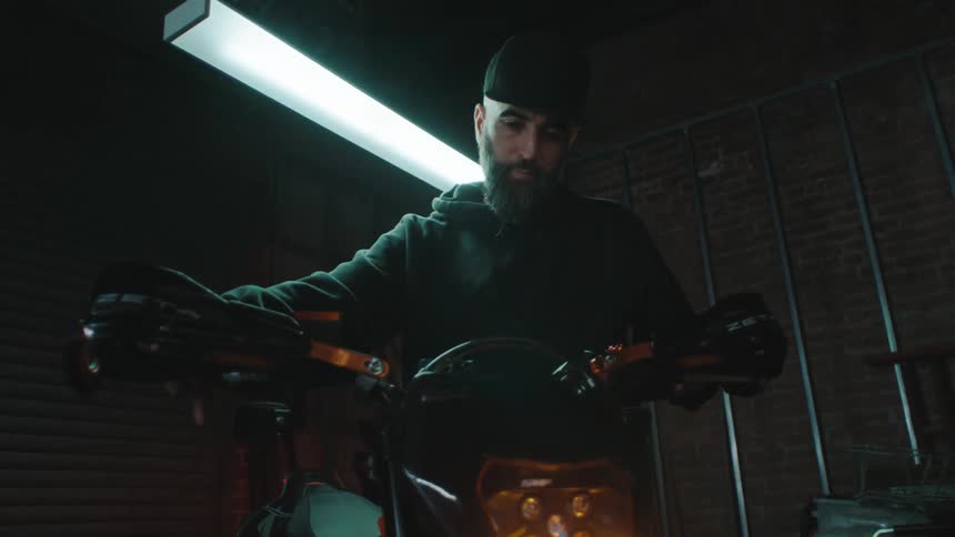 Man in a garage turning on the headlights of a motorcycle