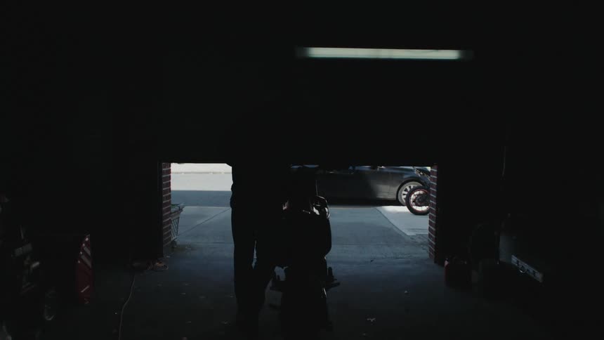A man pushes his motorcycle out of the garage