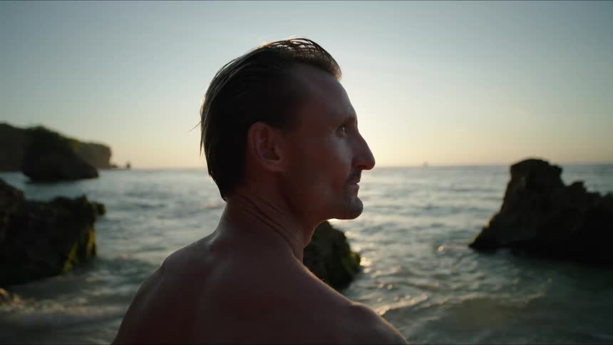 A man is turned on his back looking at the sea water on a rocky coast
