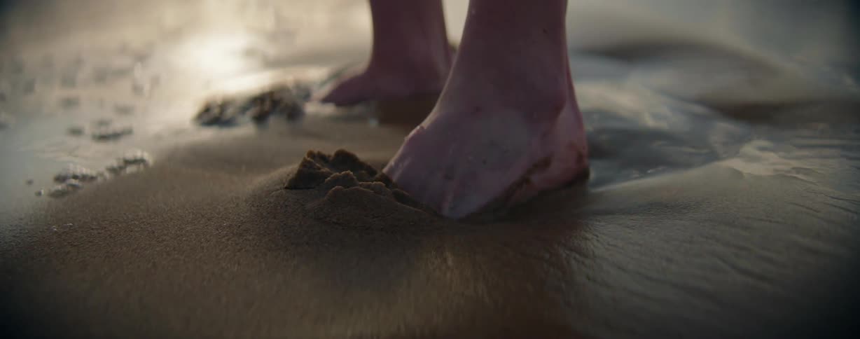 Barefoot person digs their feet into the wet beach sand