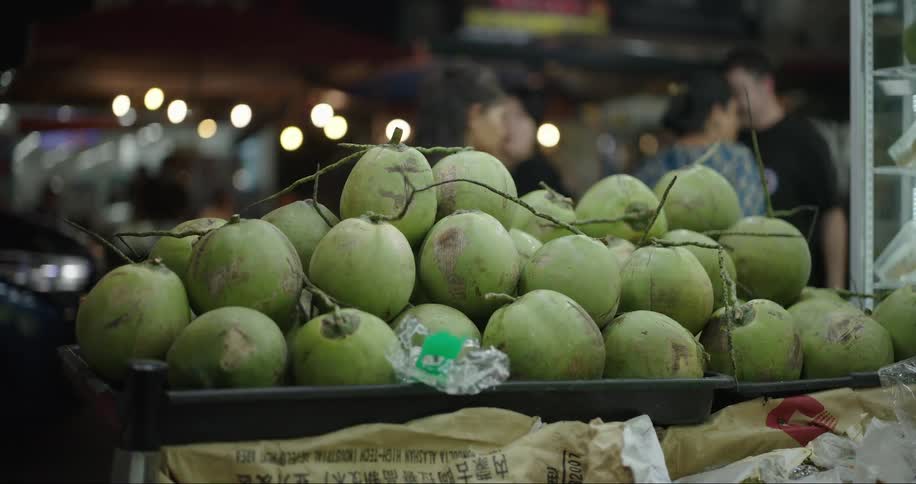 Pedestrians walk past fruit display at a street side shop during the night