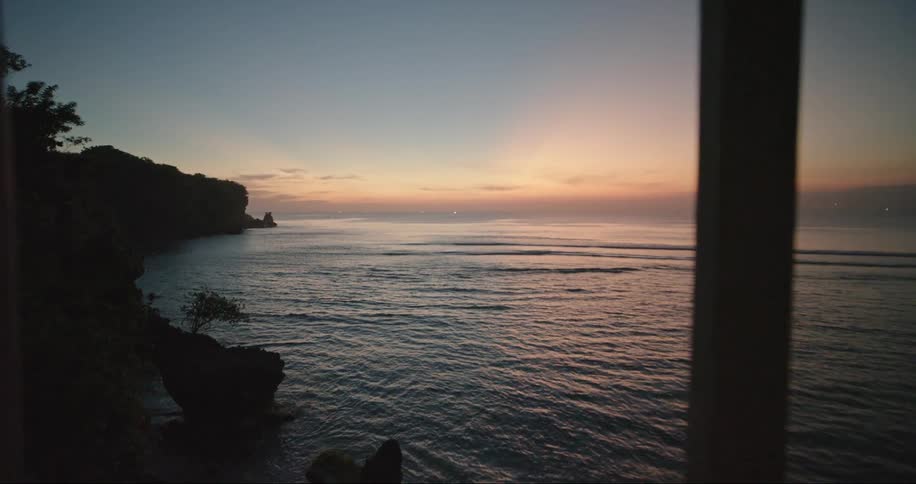 Point of view of a person opening the window overlooking the sea with its purple and reddish dawn