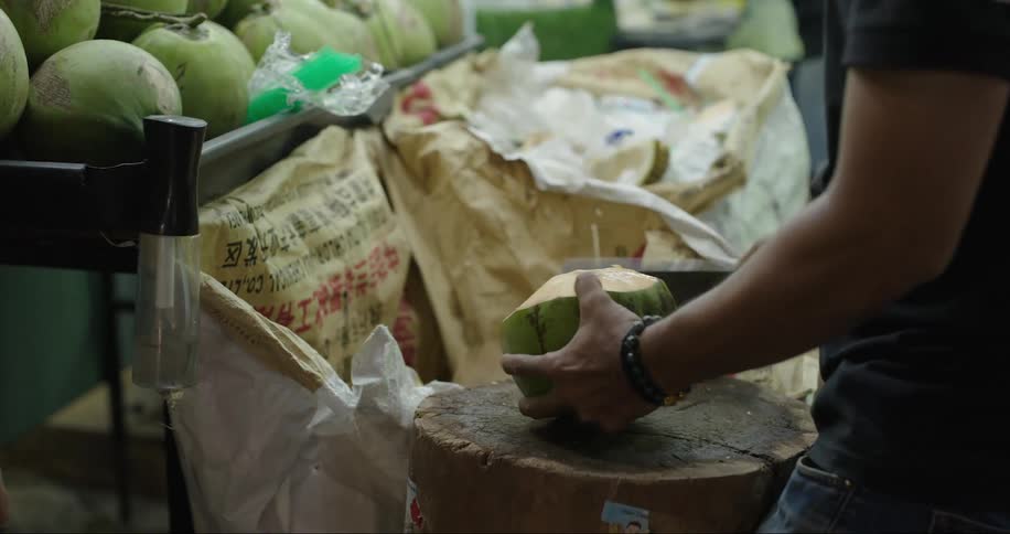 Man talking in a grocery store with another man who is cutting a coconut with a machete