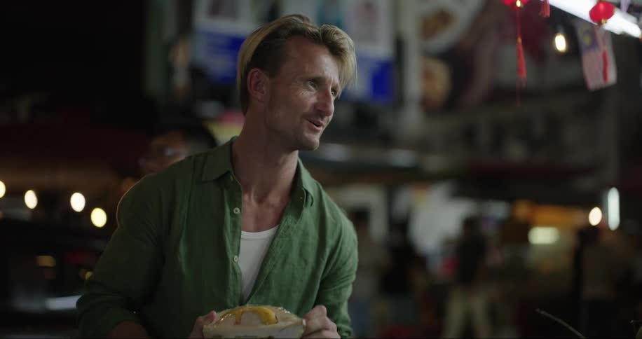 Man smiles while holding wrapped food and talking to proprietor of street side shop