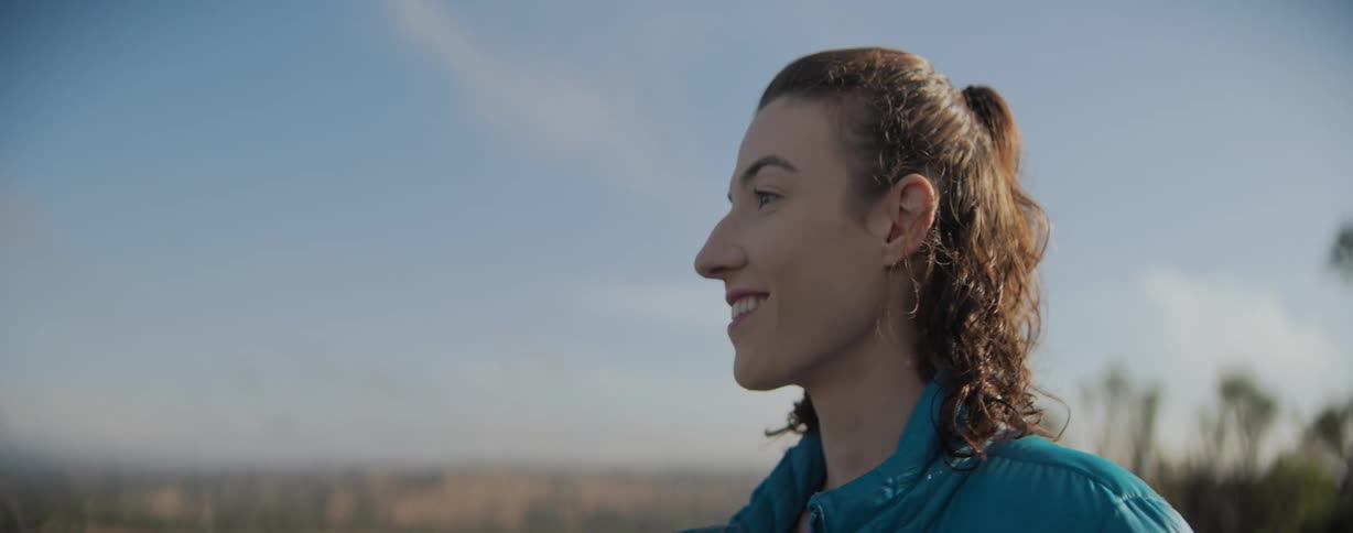 Woman with curly hair and a blue jacket smiles and looks around in the field