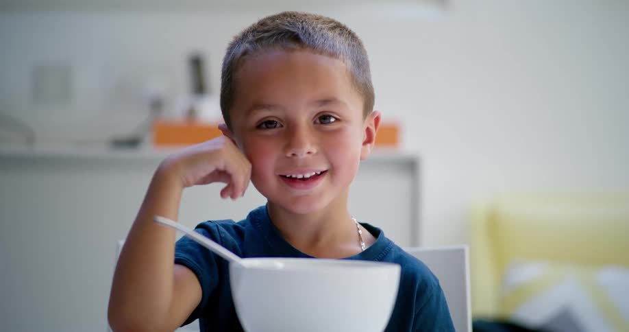 A little boy is sitting opposite a white bowl, while smiling and looking straight to camera