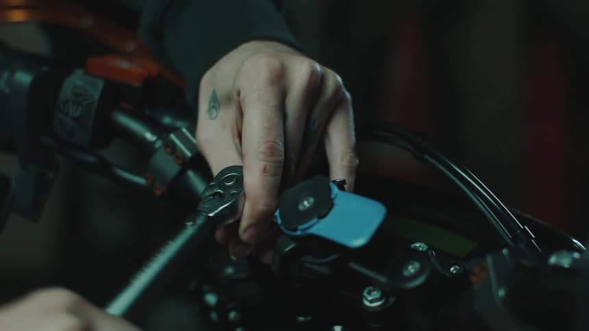 A mechanic with tattoos on his fingers uses a wrench on a motorcycle