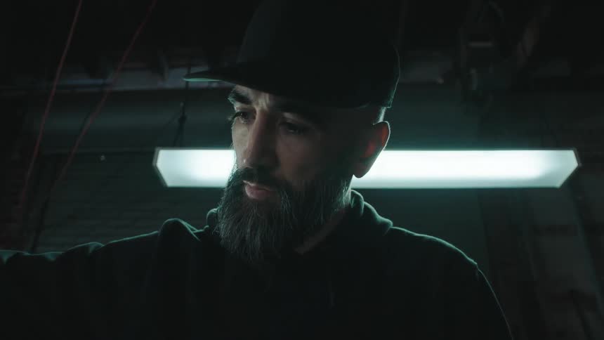 A man in a black cap and a large beard is concentrated looking at the handlebars of a motorcycle