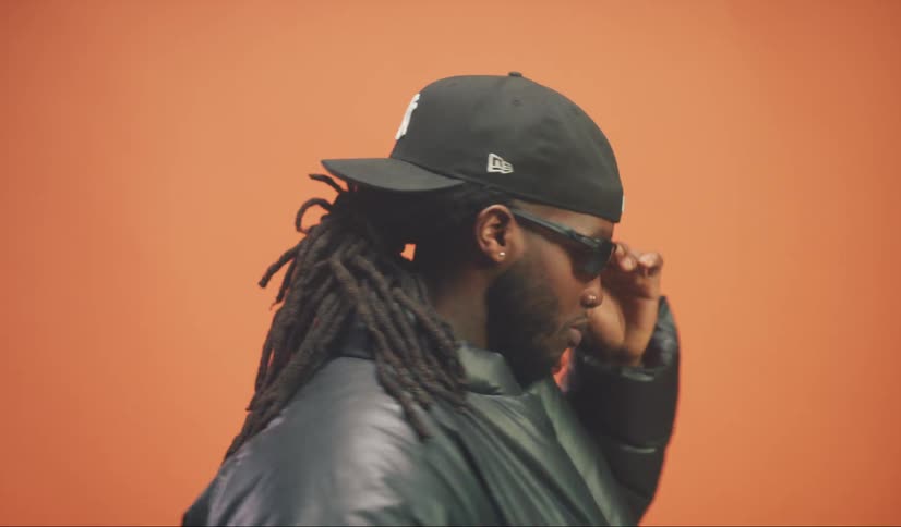 Side portrait of a man with a beard cap and sunglasses against an orange background