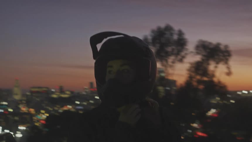 A person is taking off their helmet and they are next to a motorcycle that has the headlights on