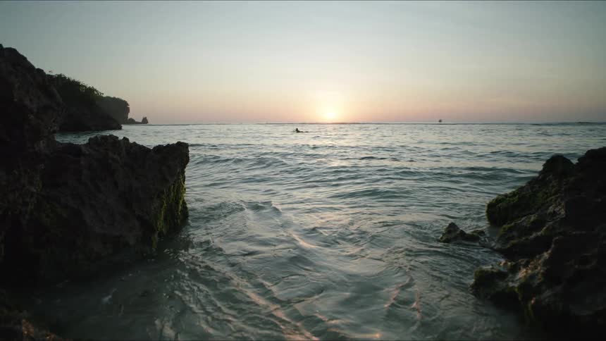 A sea coast with several rocks and some small waves breaking on them and on the horizon with the sun lighting up the sky