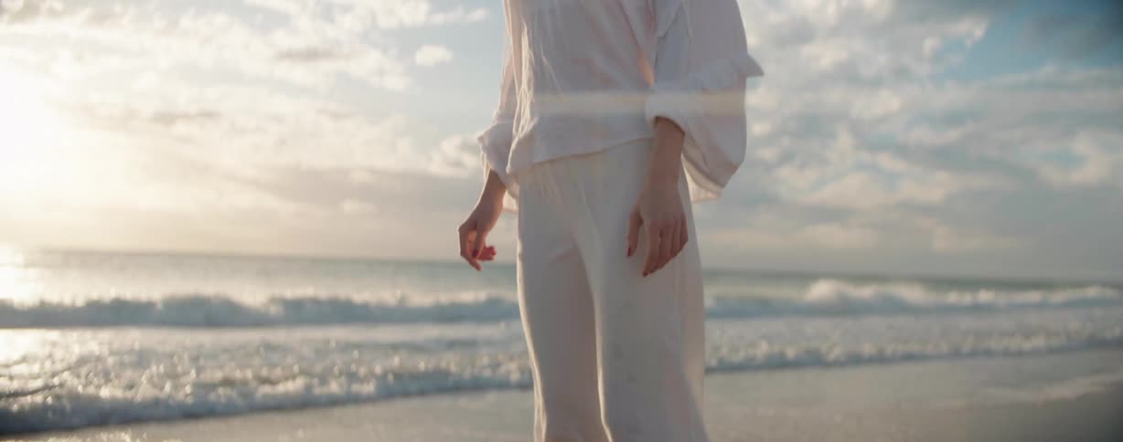 Woman standing barefoot on the beach stares toward the horizon