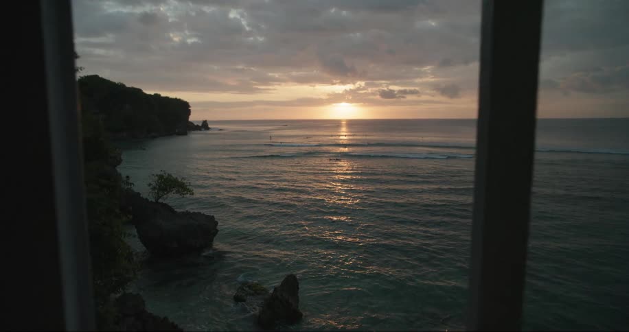 Point of view of a person walking towards the window of a seaside house with a view of the sunrise on the horizon