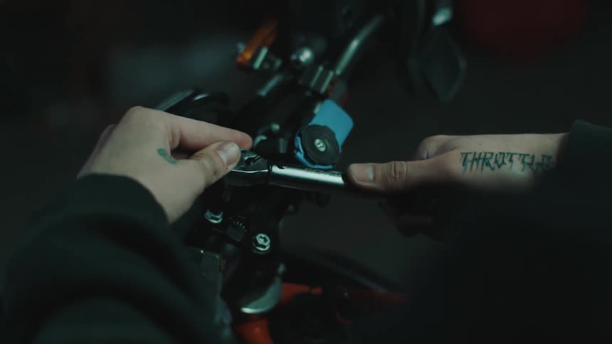 A mans hand is fixing a motorcycle with a wrench