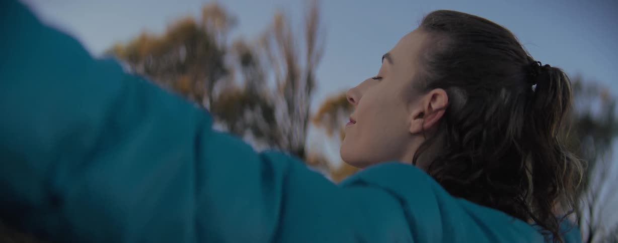 Side portrait of a young woman with her arms open in an outdoor setting